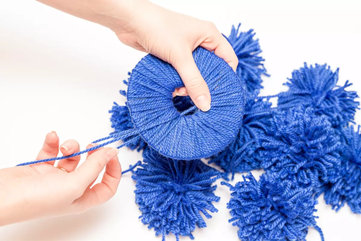 Como fazer uma decoração de aniversário simples: confira dicas! Pessoa fazendo um pompom de lã azul. Imagem ilustrativa para texto decoração de aniversário simples.